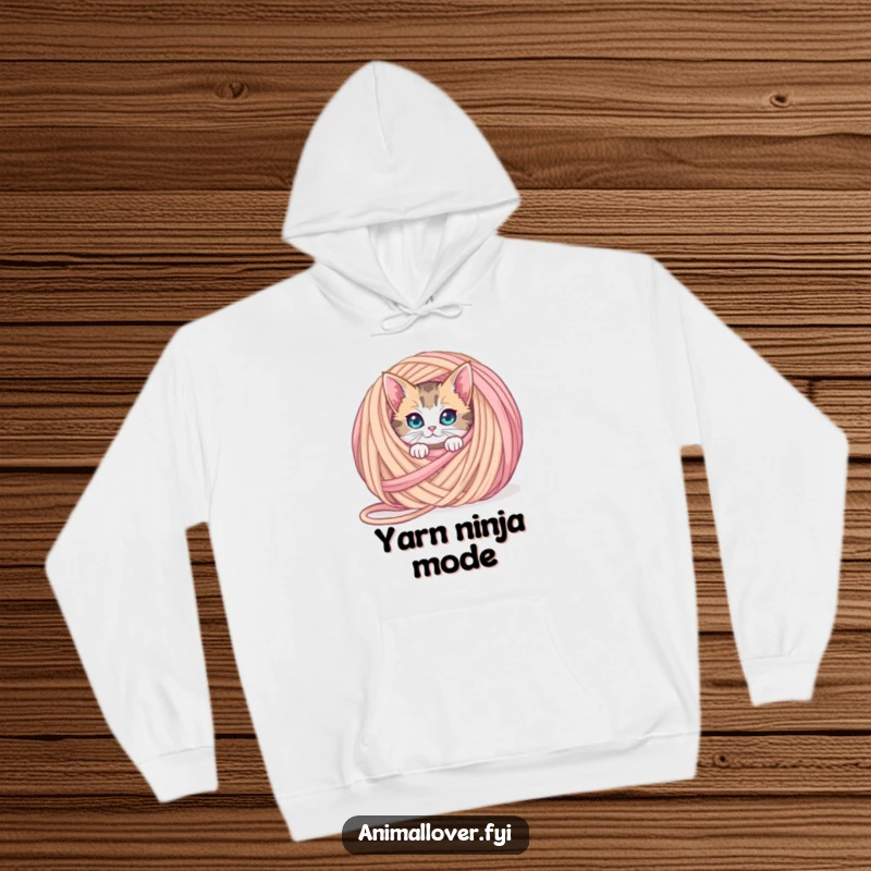 Funny curious cat hoodie peeking from behind an oversized ball of yarn, offering warmth and a touch of playful mystery.
