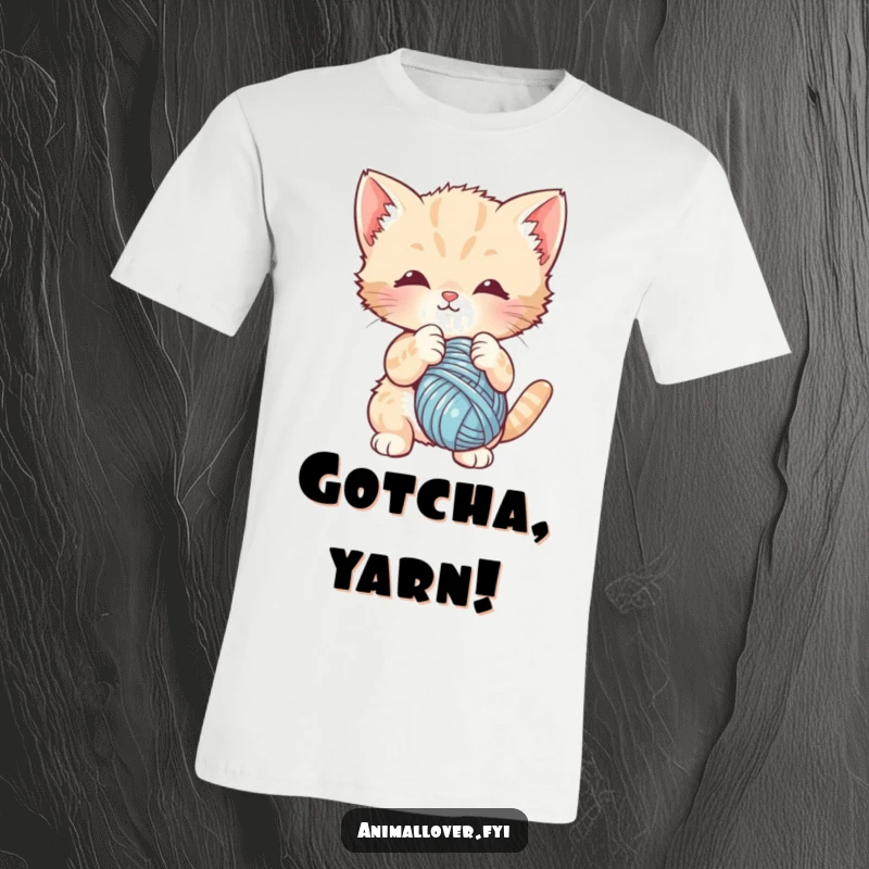 Funny t-shirt print of a cute kitten batting playfully at a dangling ball of yarn. Expresses feline joy and energy.